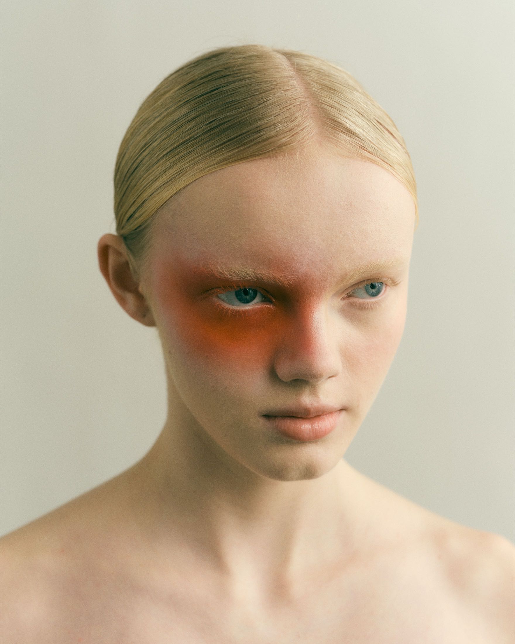 Porträt mit orangefarbenem Make-up um das linke Auge vor hellem Grund