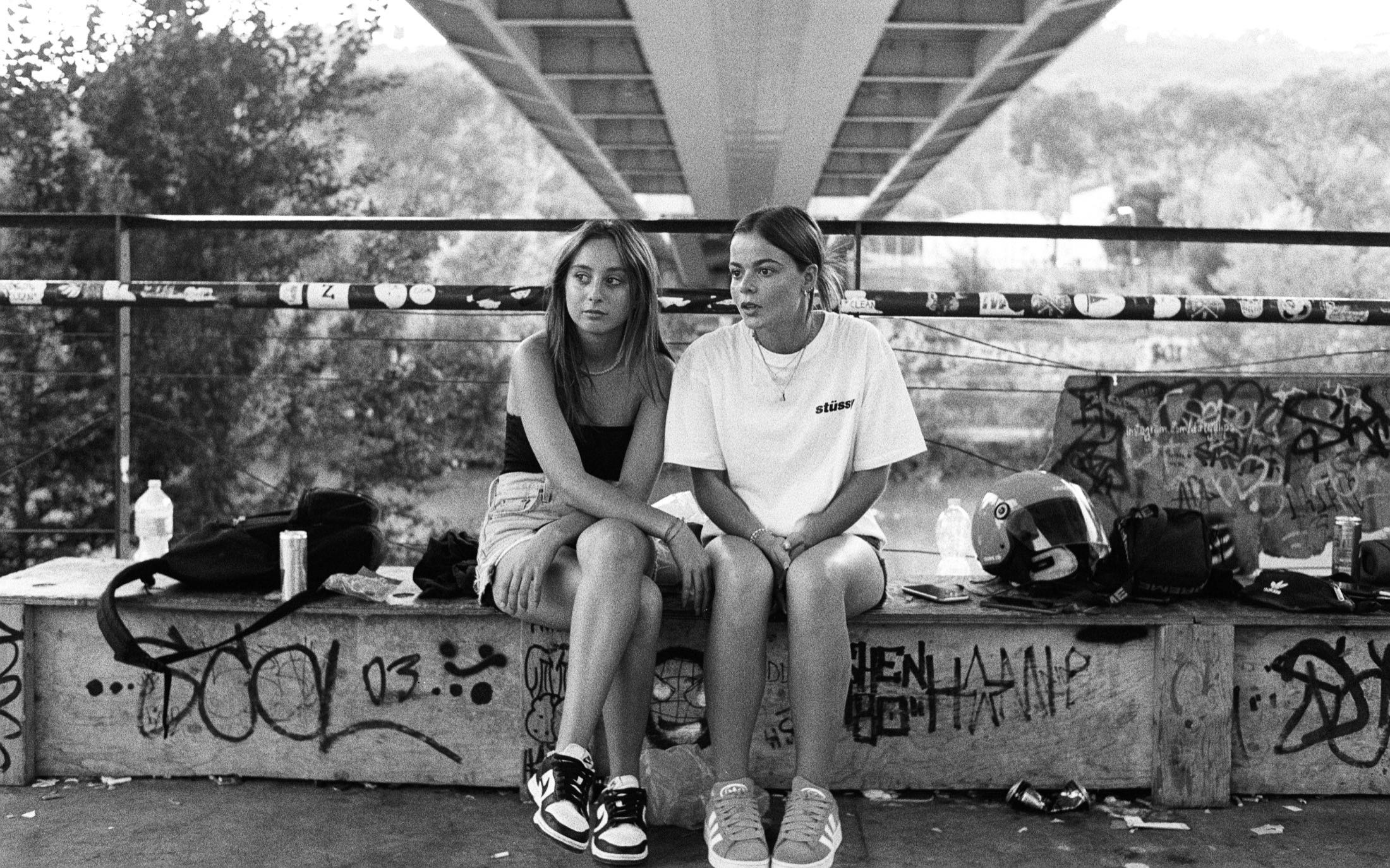 Zwei junge Frauen sitzen auf einer Graffiti-Mauer unter der Brücke