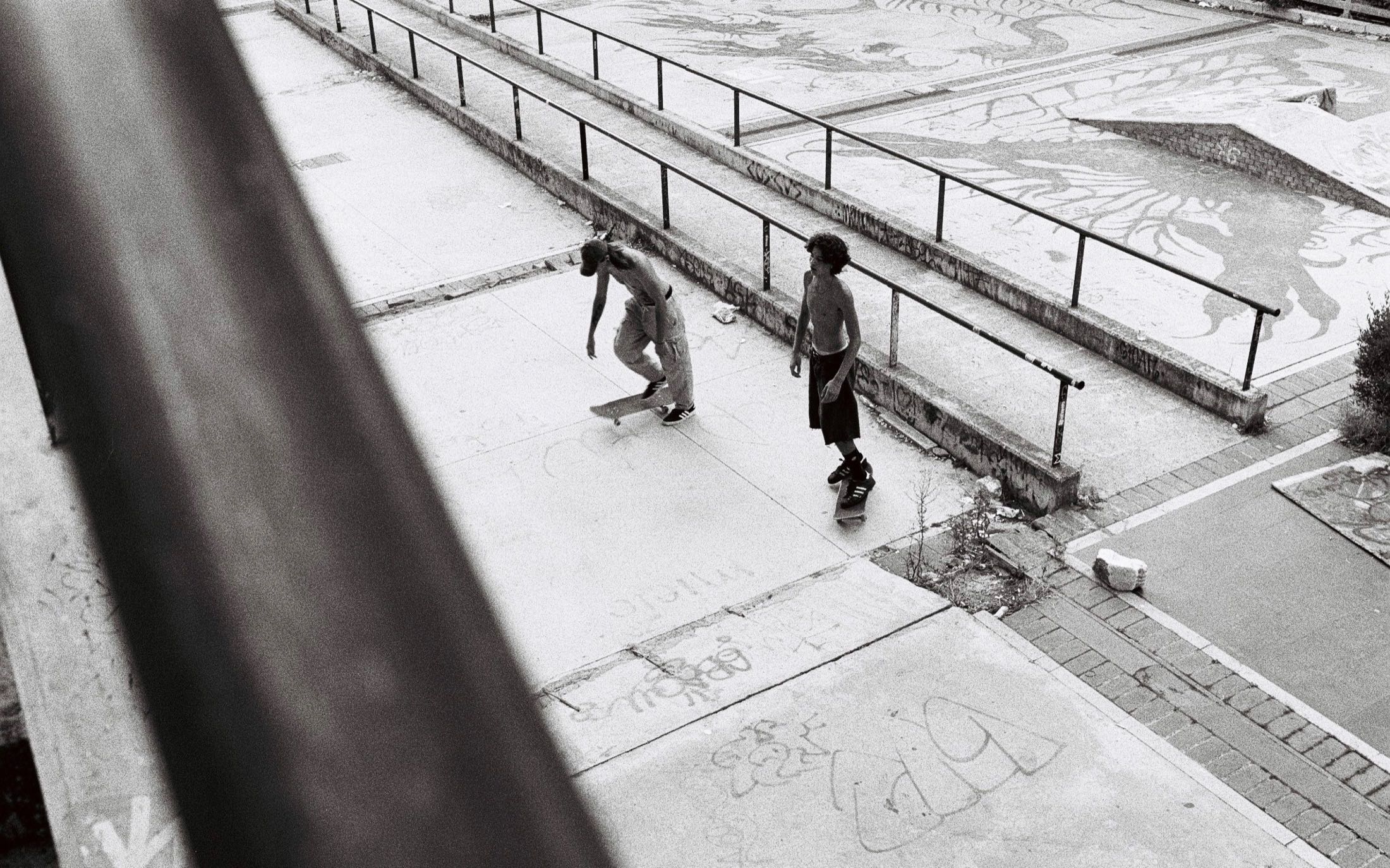 Blick von oben über ein Geländer auf zwei Skater im Park